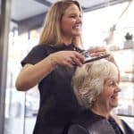 Haordresser smiling while working on the hair of an older woman.