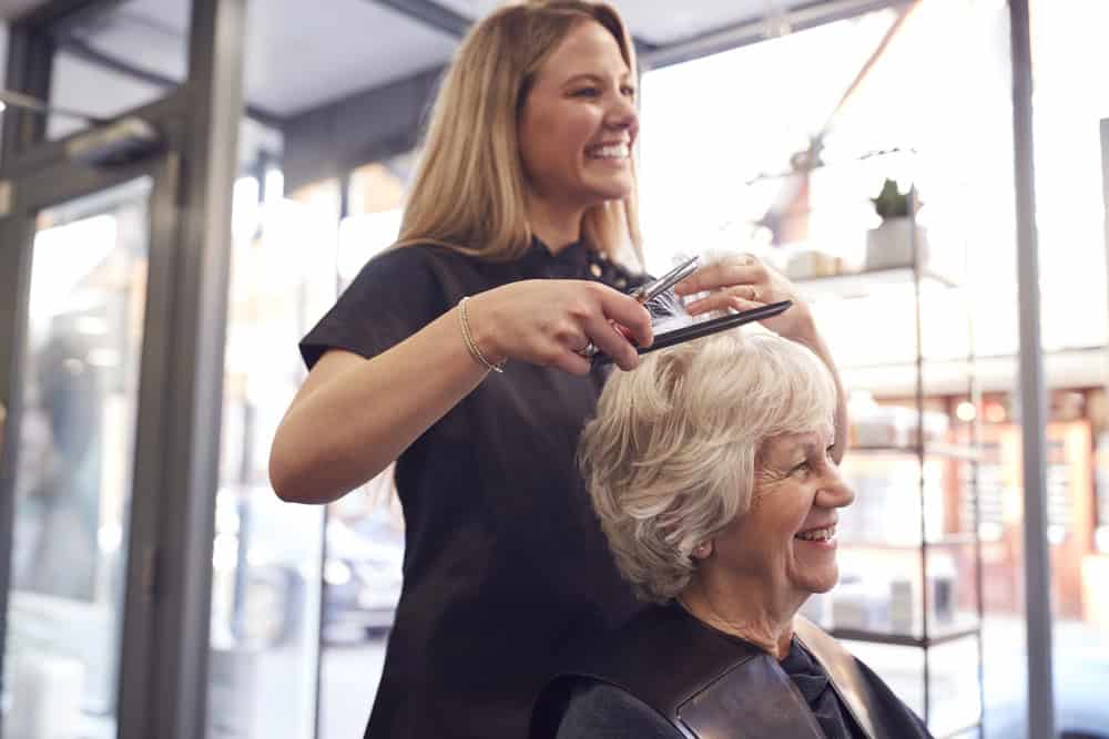 Haordresser smiling while working on the hair of an older woman.