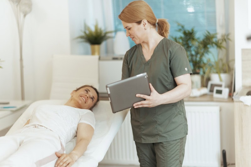 Massage therapist and patient discussing more service options while the patient lies on the massage table.